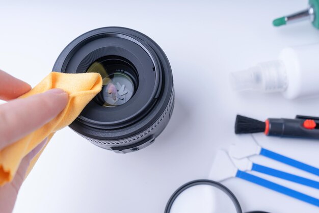 La mano del fotógrafo con microfibra amarilla limpia la lente de la cámara. Fondo blanco