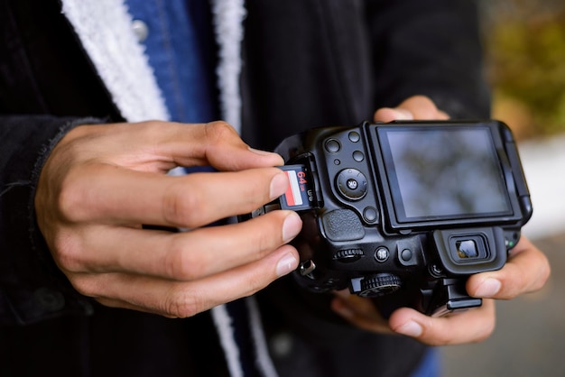 La mano del fotógrafo sostiene la tarjeta de memoria flash cerca de la cámara réflex digital profesional