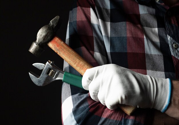 Mano fuerte de manitas en primer plano de guantes con herramientas de martillo y llave.