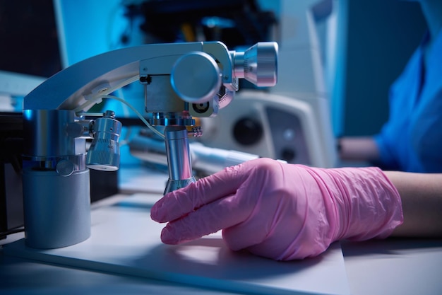 Mano con guante ajustando un micromanipulador bajo un microscopio en el laboratorio