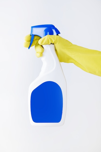 Foto la mano en el guante amarillo tiene una botella de spray de detergente líquido sobre fondo blanco.