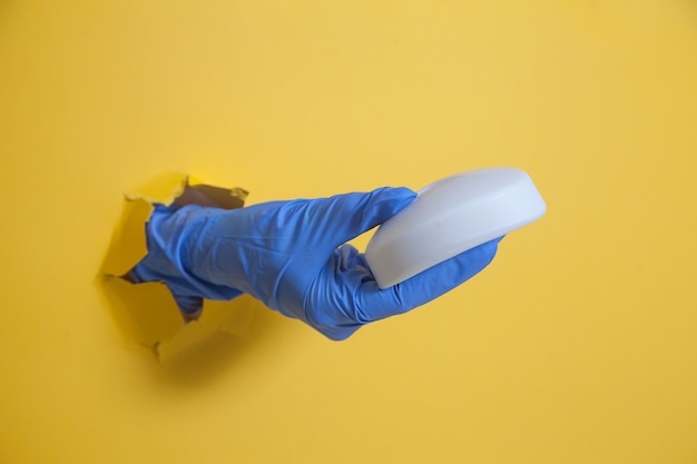 Foto una mano en un guante azul de un agujero sobre un fondo amarillo tiene un jabón blanco