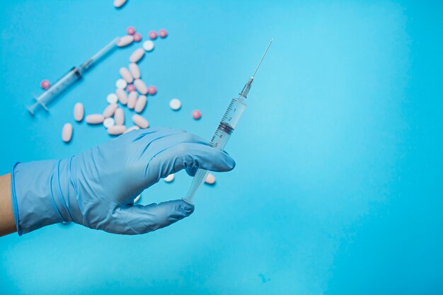 Una mano en un guante azul sostiene una jeringa. El doctor sostiene una jeringuilla para la vacunación. Medicina. Fondo azul, lugar para el texto. Copia espacio