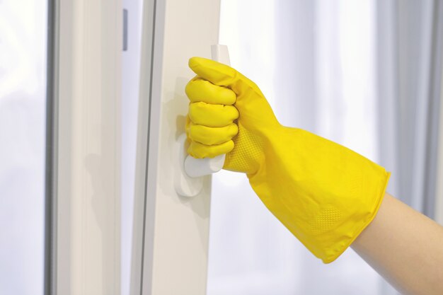 La mano en el guante de goma amarillo protector abre y cierra la ventana de plástico, PVC