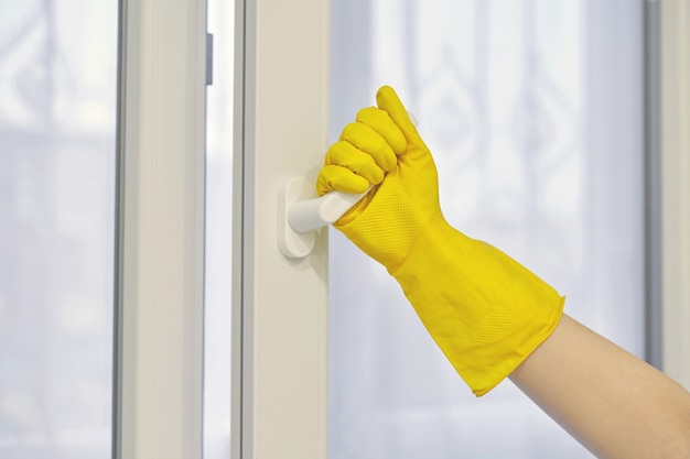 La mano en el guante de goma amarillo protector abre y cierra la ventana de plástico PVC