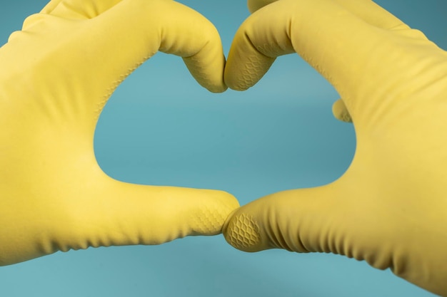Mano en guante de goma amarillo sostiene esponja para lavar platos y limpiar mano aprieta esponja en puño sobre fondo azul