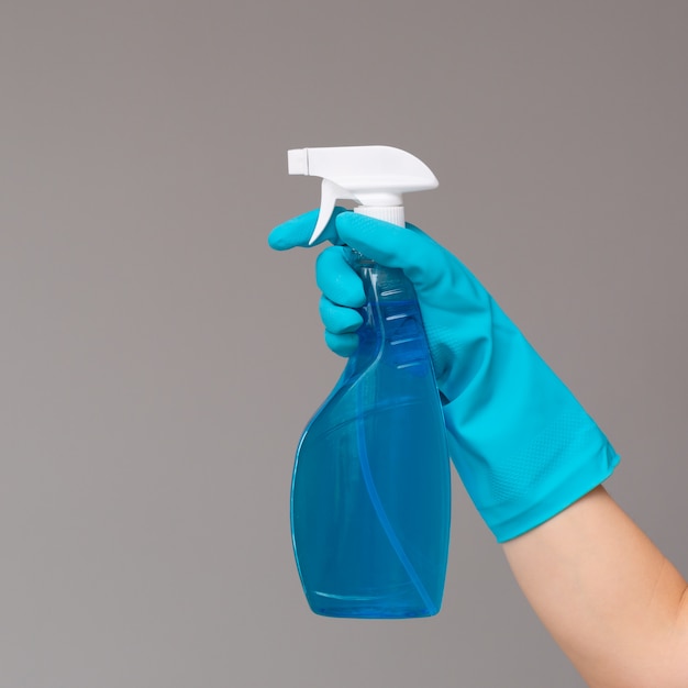 Una mano en guante de goma azul sostiene el limpiacristales en una botella de spray