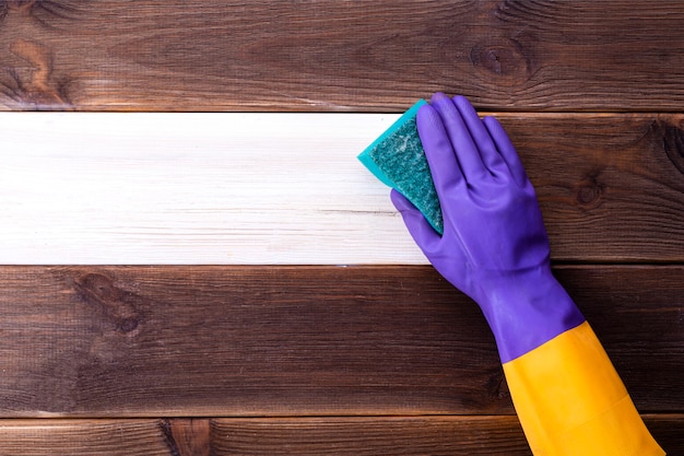 Una mano en un guante de goma lava una superficie de madera. Limpieza, limpieza de habitaciones.