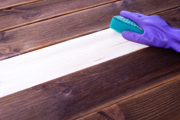 Una mano en un guante de goma lava una superficie de madera. Limpieza, limpieza de habitaciones.