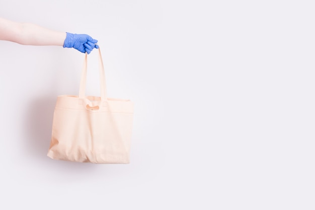 Una mano en un guante de goma médica desechable azul sostiene una bolsa de compras para ir de compras