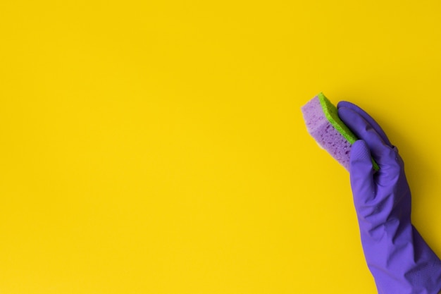 De la mano en un guante de goma morado sobre un fondo amarillo. Concepto de limpieza, servicio de limpieza. Bandera. Endecha plana, vista superior