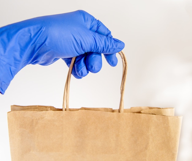 Una mano en un guante de goma sostiene una bolsa de papel, entrega de alimentos en un embalaje ecológico, cero desperdicio