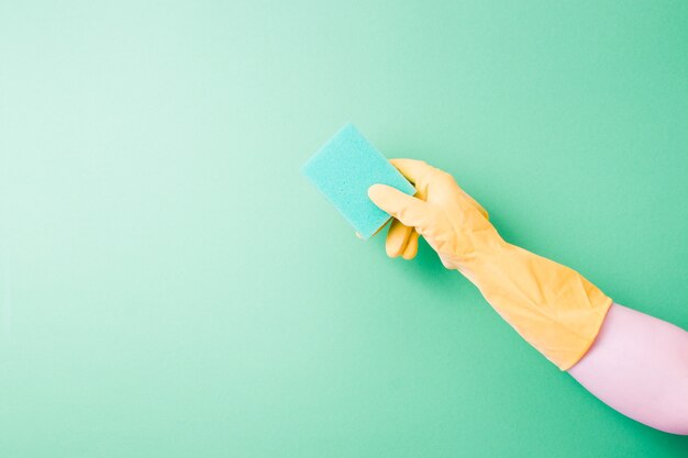 Una mano en un guante de goma sostiene una esponja verde fondo verde