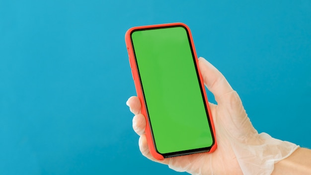 La mano en un guante de goma sostiene un teléfono inteligente con una pantalla verde