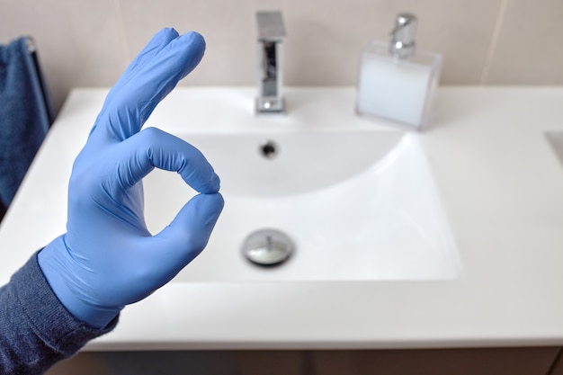 Mano con un guante de látex azul en un baño haciendo el símbolo OK