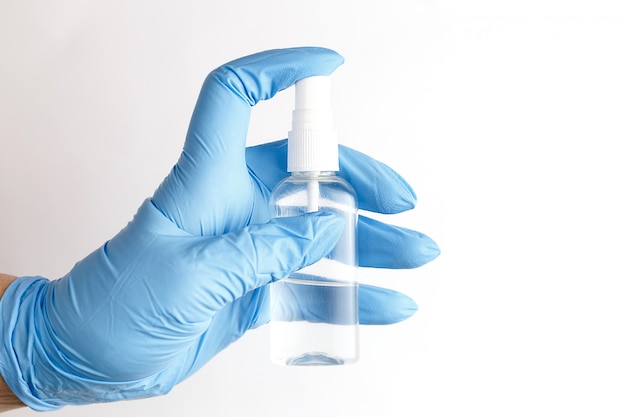Una mano en un guante médico azul desechable contiene un antiséptico en forma de aerosol, una solución de alcohol para desinfectar superficies, higiene y prevención de enfermedades virales.