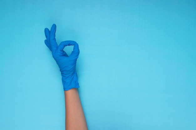 Mano en guante médico azul haciendo gesto de mano sobre fondo azul claro