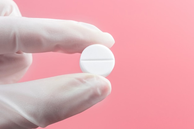 Una mano en un guante médico blanco sostiene un primer plano de la píldora sobre un fondo rosa. Atención médica, medicina, tratamiento, concepto de terapia.