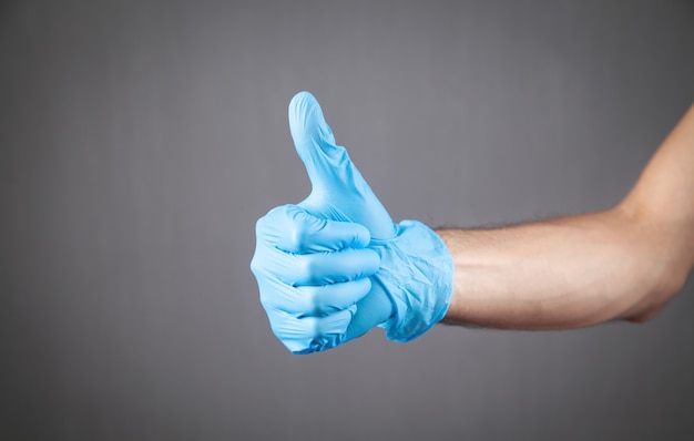 Mano en guante médico haciendo gesto con el pulgar hacia arriba.