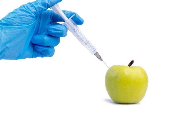 Una mano en un guante médico inserta una jeringa en una manzana verde sobre un fondo blanco Aditivos alimentarios nocivos Concepto nitratos pesticidas OMG