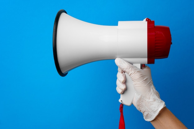 Mano en guante médico sosteniendo el altavoz contra la superficie azul