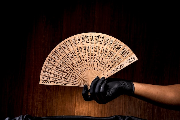 Mano con guante negro sosteniendo un abanico chino sobre un fondo de madera oscura enfoque selectivo