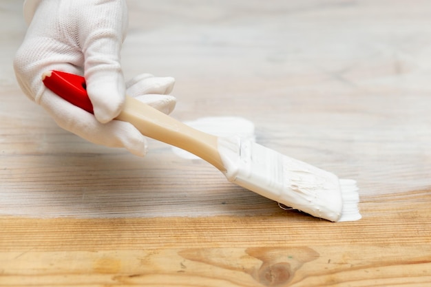 Una mano en un guante protector con un cepillo pinta muebles de madera