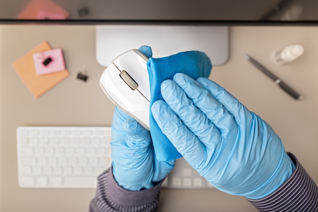Mano con guante protector limpiando un mouse de computadora con desinfectante. concepto de prevención Vista superior