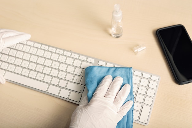 Mano con guante protector limpiando un teclado con desinfectante. Concepto de prevención de contaminación por brote de coronavirus COVID-19