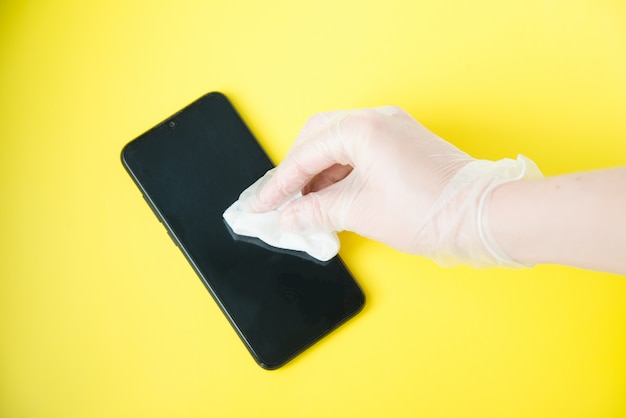 Foto mano en guante protector con servilleta de limpieza del teléfono móvil sobre fondo amarillo. concepto de desinfección de coronavirus.