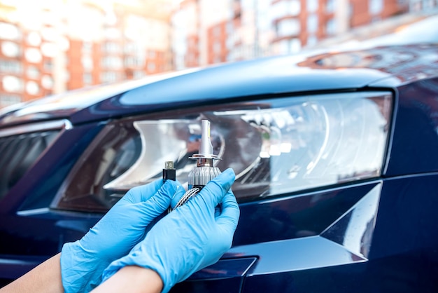 La mano en un guante sostiene dos lámparas de gelagon contra el fondo de un automóvil nuevo y un faro de automóvil Concepto de reparación de automóviles