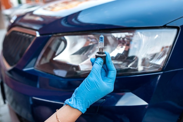 La mano en un guante sostiene dos lámparas de gelagon contra el fondo de un automóvil nuevo y un faro de automóvil Concepto de reparación de automóviles