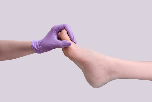 La mano en el guante sostiene la pierna femenina después de la pedicura. Aislar