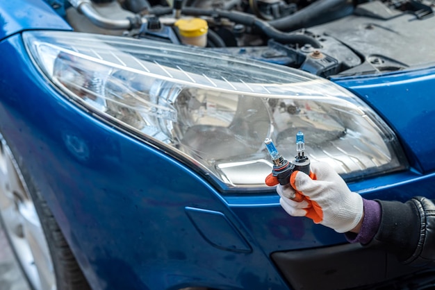 Mano en guantes especiales tiene lámparas de gelagón cerca de los faros de un hermoso auto. Concepto mecánico. Concepto de lámpara Gelagon