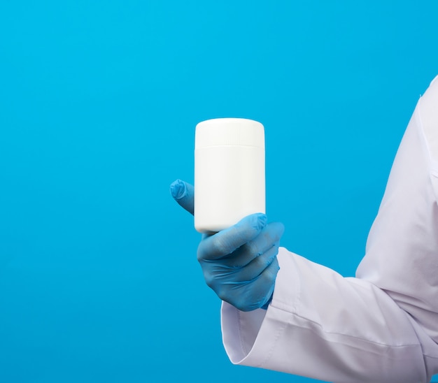 La mano en guantes estériles azules sostiene un frasco de plástico blanco para píldoras, concepto de tratamiento médico para enfermedades
