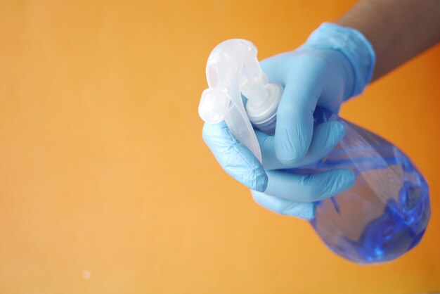 Mano en guantes de goma azul con botella de spray