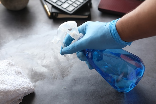 Mano en guantes de goma azul sosteniendo la mesa de limpieza de botellas de spray