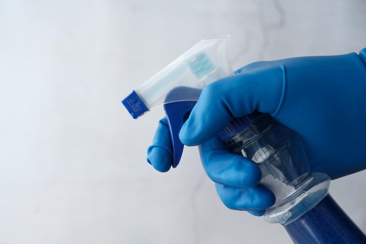Foto mano en guantes de goma azules sosteniendo botella de pulverización
