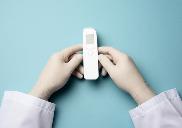Mano en guantes de látex blancos sostienen un termómetro electrónico para medir la temperatura, dispositivo sin contacto