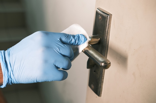 Mano en guantes limpiando la perilla de la puerta con alcohol