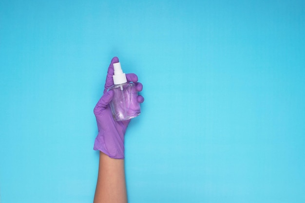 Mano en guantes médicos de color lila con spray desinfectante sobre fondo azul claro