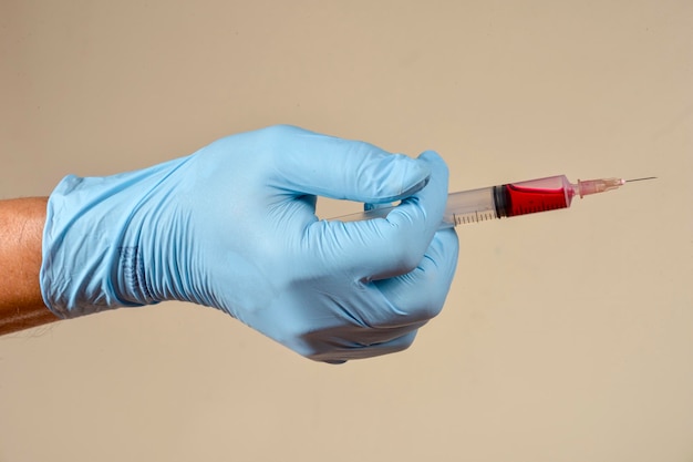 Mano con guantes protectores sosteniendo un objeto médico en un fondo marrón claro