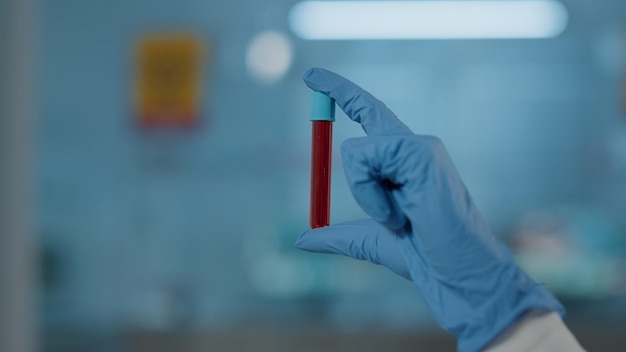 Foto mano con guantes sosteniendo el tubo de ensayo en el laboratorio de ciencias, analizando la sustancia del adn para el experimento de biología. especialista en microbiología que trabaja con cristalería y líquido rojo en matraz. de cerca