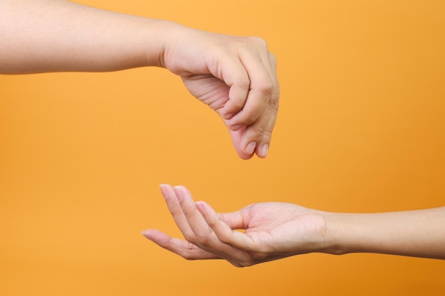 La mano hace un gesto dando caridad o donación a la otra mano aislada en fondo amarillo