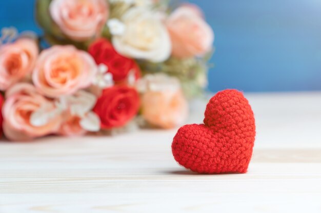 mano hacer hilo corazón rojo delante de ramo de flores color de rosa en mesa de madera