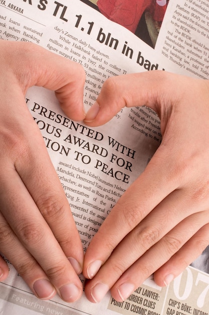 Foto mano haciendo una forma de corazón en un periódico