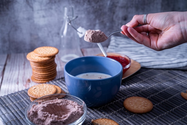 Mano haciendo leche de cacao con cacao en polvo en una taza junto a las galletas María (galletas María)