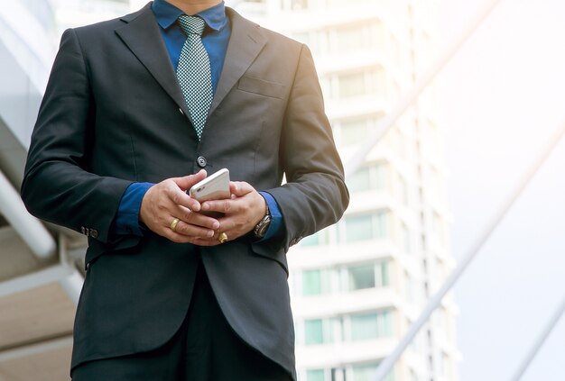 Mano hermosa del hombre de negocios que sostiene el teléfono móvil o el teléfono elegante en ciudad moderna.