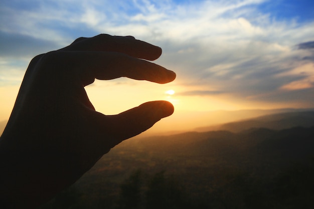 Mano hermosa silueta en sol y puesta de sol en la montaña. concepto de poder y esperanza.