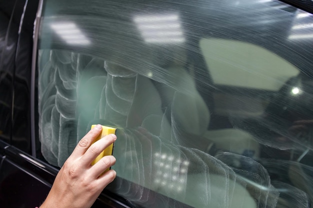 La mano del hombre aplica un limpiador desengrasante con una esponja amarilla en la ventana lateral del camión para aplicar un revestimiento protector de nanocerámica Industria de servicios automotrices